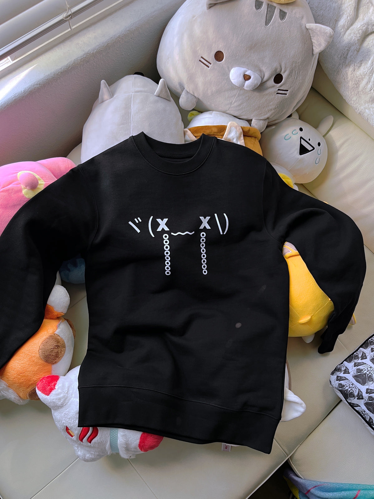 A soft black cotton sweatshirt featuring a crying emoticon on top of a pile of plushies