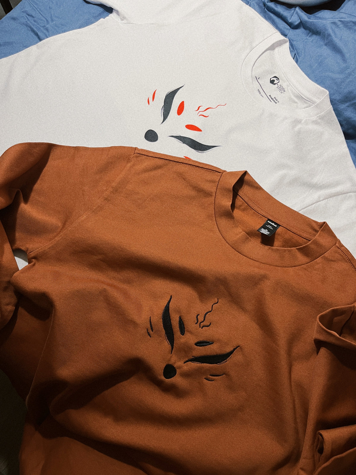 Premium white cotton T-shirt featuring a minimal black and red markings of a kitsune, next to a matching long-sleeve