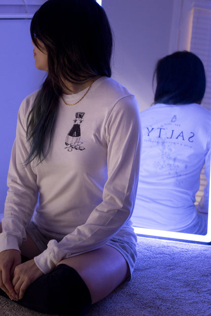 Female model wearing a white cotton long-sleeve crewneck featuring a sassy soy sauce bottle and edamame on the front and the word "SALTY" with salt on the back, reflected in a mirror