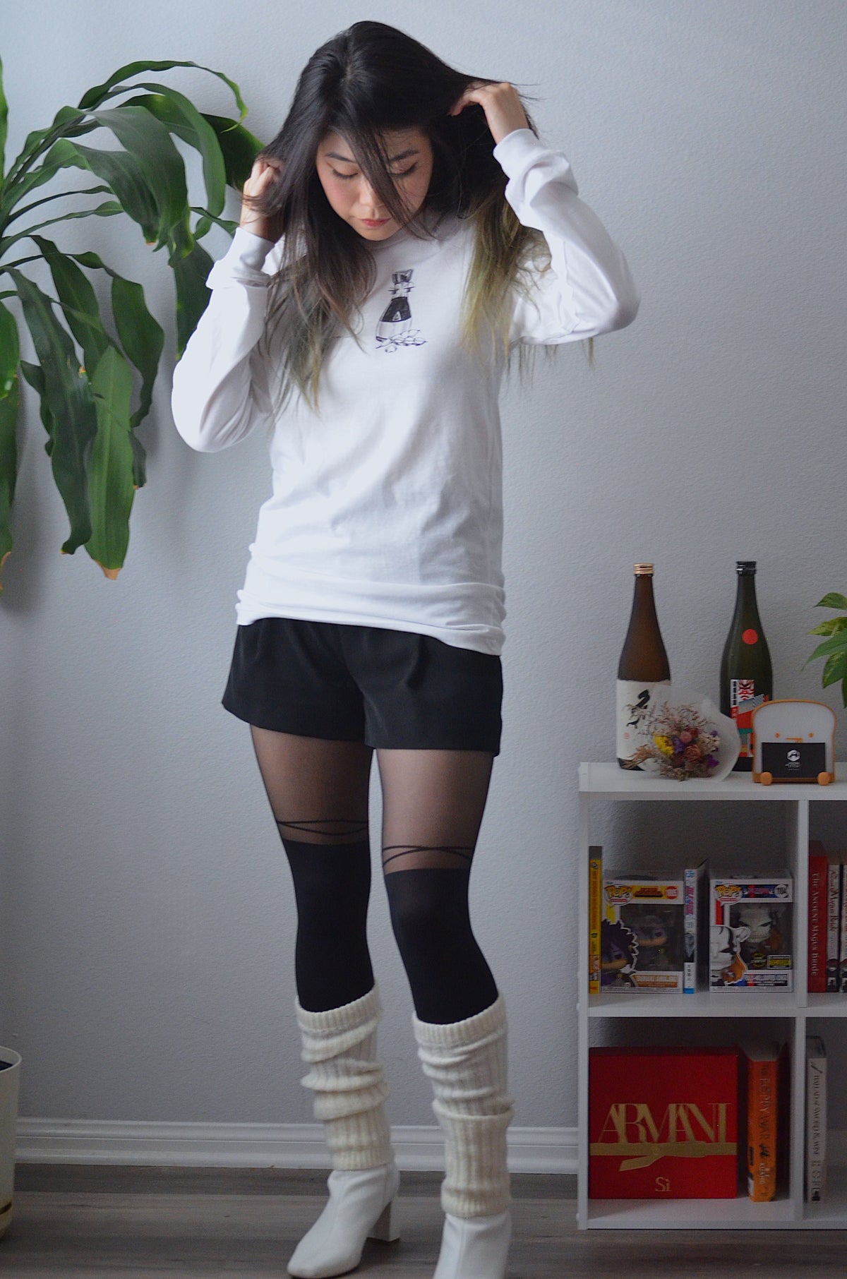 Female model wearing a white cotton long-sleeve crewneck featuring a sassy soy sauce bottle and edamame on the front, paired with black shorts, white booties, and white leg warmers